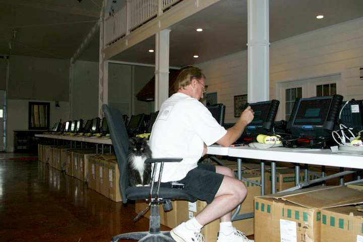 a long row of unboxed equipment set up on tables, a man working on them