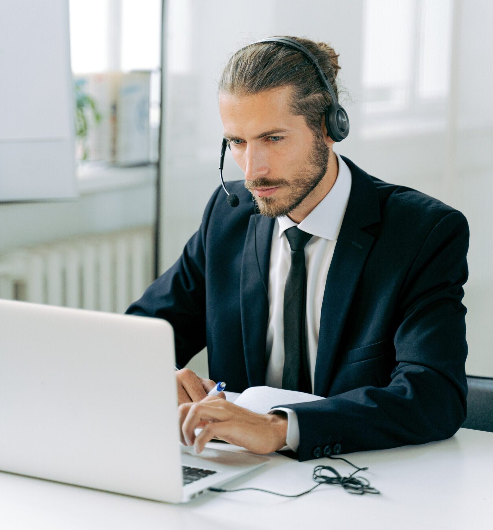 a businessman at a desk wearing a headset with a microphone looking at a laptop