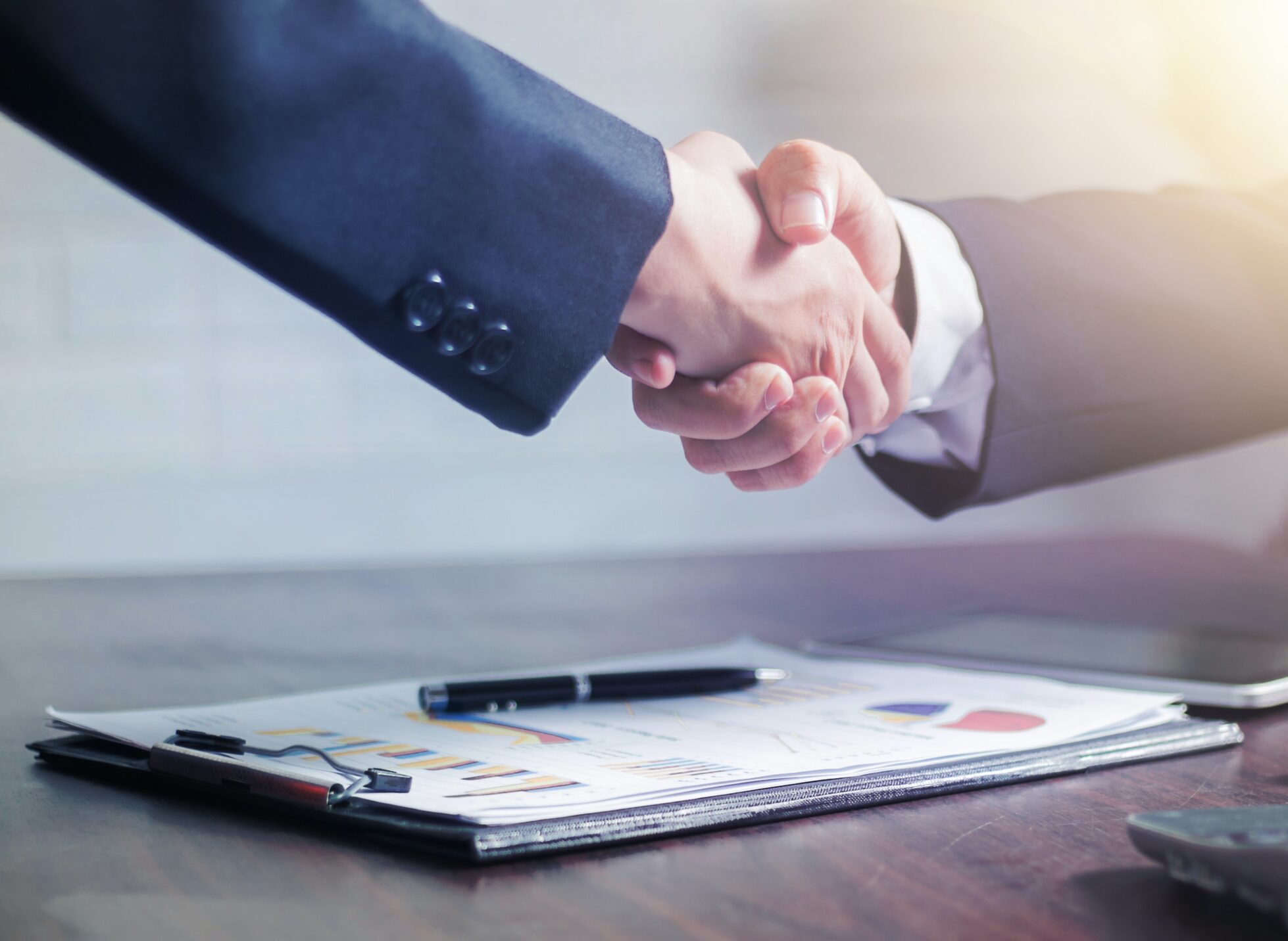 two business people shaking hands over documents and a pen